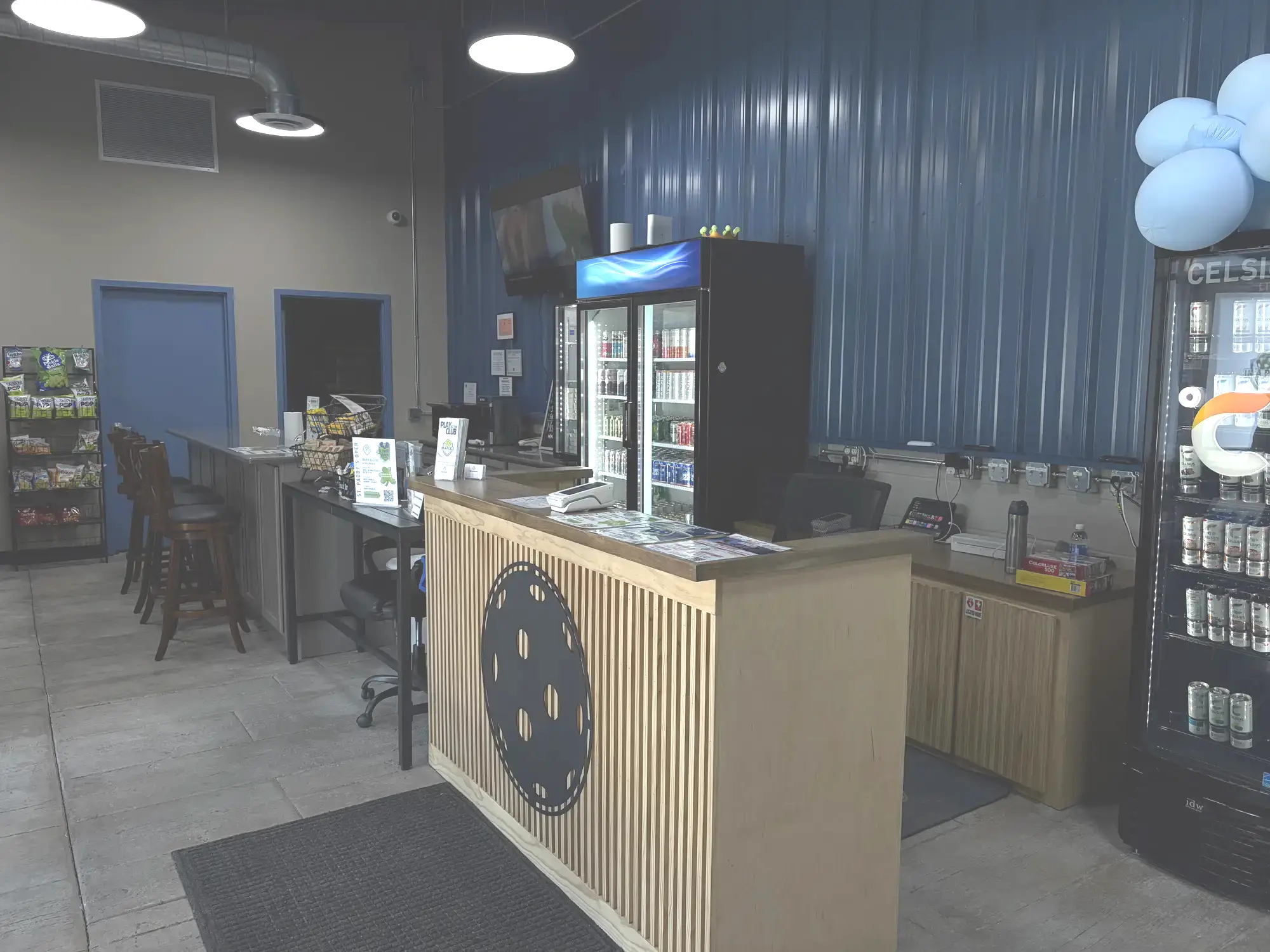 Front desk and bar area with beverage coolers, In A Pickle logo on the counter, and snack display