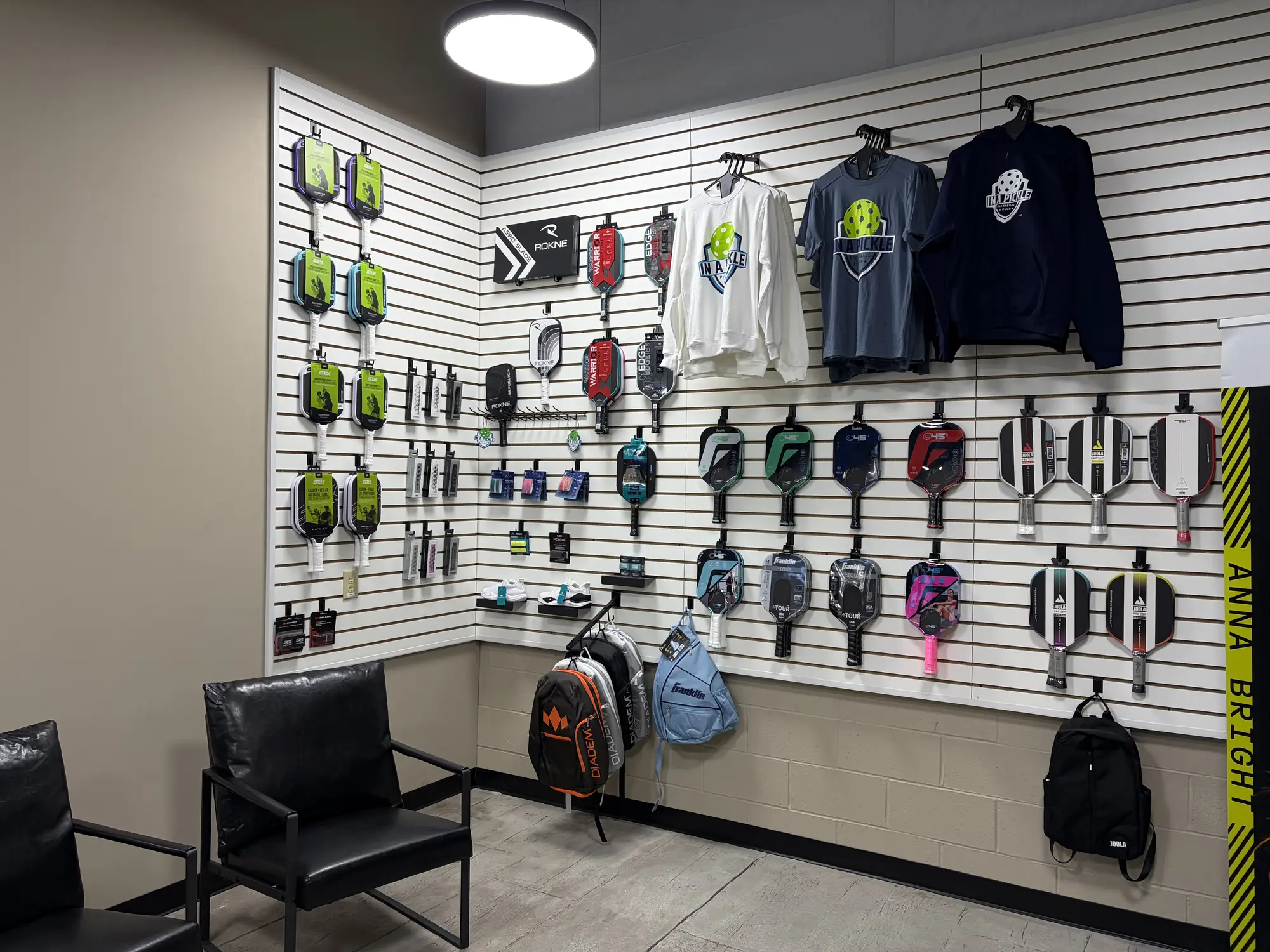 Pro shop wall display with pickleball paddles, bags, apparel, and In A Pickle branded gear