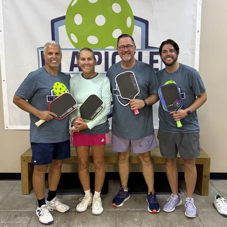 Four players holding paddles in front of the club banner